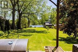 Expansive grassy lawn extending towards a body of water, bordered by mature trees and lush foliage - 