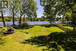 Expansive waterfront lawn with mature trees and a stone-lined fire pit - 