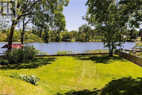 Expansive lakeside property featuring a large grassy lawn, mature shade trees, and a wooden privacy fence - 100 Mechanic Street W, Waterford, ON - Outdoor With Body Of Water With View