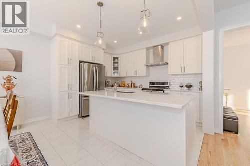 Kitchen with appliances with stainless steel finishes, an island with sink, white cabinetry, and wall chimney range hood - 53 Mackay Drive, Woodstock, ON - Indoor Photo Showing Kitchen With Upgraded Kitchen