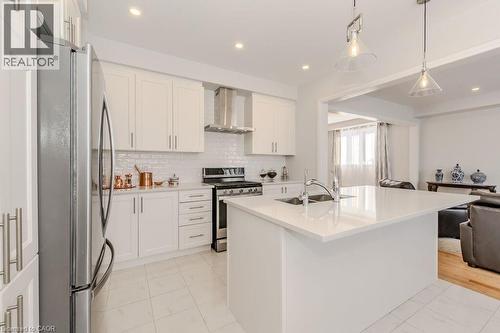 Kitchen featuring sink, wall chimney exhaust hood, an island with sink, white cabinets, and appliances with stainless steel finishes - 53 Mackay Drive, Woodstock, ON - Indoor Photo Showing Kitchen With Double Sink With Upgraded Kitchen