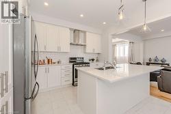 Kitchen featuring sink, wall chimney exhaust hood, an island with sink, white cabinets, and appliances with stainless steel finishes - 