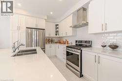 Kitchen featuring white cabinets, wall chimney range hood, sink, light tile patterned flooring, and stainless steel appliances - 