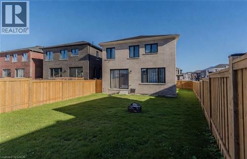 Spacious backyard featuring a manicured lawn, full perimeter wood fencing, a light brick exterior, and multiple rear windows including a sliding glass door - 53 Mackay Drive, Woodstock, ON - Outdoor