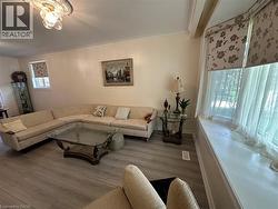 Spacious living area featuring wood-finish flooring, a bay window with a built-in window seat, crown molding, and a decorative ceiling light fixture - 