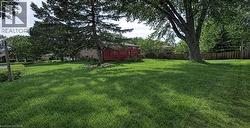 Expansive rear yard featuring a verdant lawn, mature trees providing natural shade, a privacy fence, and a visible red deck structure - 