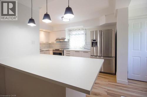 Kitchen featuring a spacious white countertop island, stainless steel refrigerator, white cabinetry, subway tile backsplash, and light wood-finish flooring - 30 Eastvale Place, Hamilton, ON - Indoor Photo Showing Kitchen