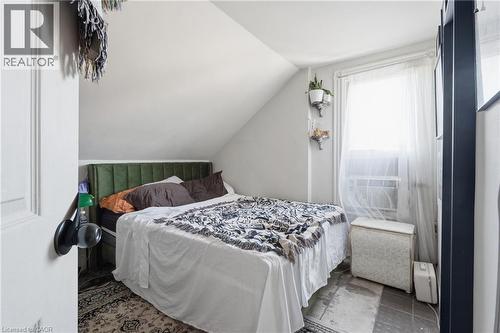 Sloped ceiling room featuring a window with sheer curtains, a dark-framed built-in element, and patterned area rugs over a tiled floor - 355 Barton Street E, Hamilton, ON - Indoor Photo Showing Bedroom