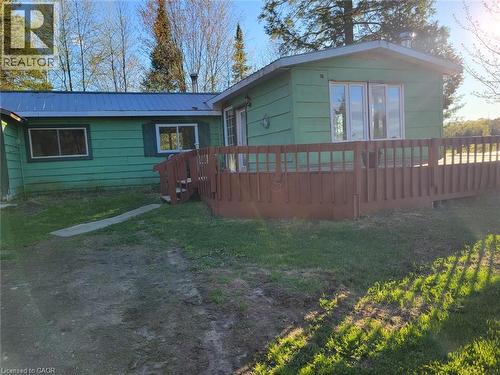 Wood-sided exterior featuring a metal roof, an elevated wooden deck with railings, multiple windows, and a partially grassed lawn - 1006 Hurdville Road, Mckellar, ON - Outdoor