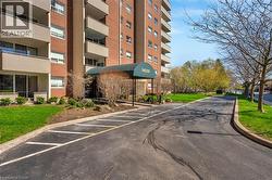 Brick facade multi-story building featuring individual balconies, a covered entrance with a numbered awning, and a paved parking area - 