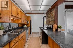 U-shaped kitchen featuring wood cabinetry, dark countertops, stainless steel appliances, and a stacked stone accent wall - 