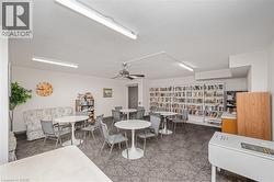 Community room featuring expansive built-in bookshelves, patterned carpet flooring, and multiple round tables with seating - 