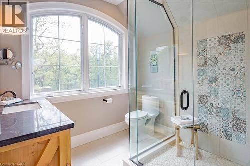Bathroom with arched window, wood-finish vanity with countertop, glass-enclosed shower with pebble flooring, and decorative tiled shower wall - 1521 Emily Lane, Severn, ON - Indoor Photo Showing Bathroom