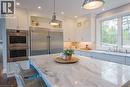 Kitchen featuring a spacious island with a natural stone countertop, white shaker cabinetry, stainless steel double ovens, a stainless steel refrigerator, and ample natural light from large windows - 1521 Emily Lane, Severn, ON  - Indoor Photo Showing Kitchen With Upgraded Kitchen 