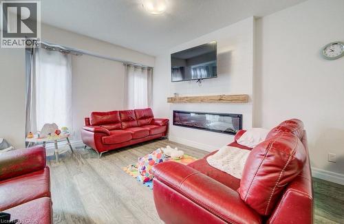 Living area featuring light wood-finish flooring and multiple windows with curtain rods - 32 Faith Street Unit# 19, Cambridge, ON - Indoor Photo Showing Living Room With Fireplace