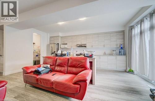 Open-concept living space featuring wood-finish flooring, a full kitchen with light-toned cabinetry and stainless steel appliances, and large windows with privacy drapes - 32 Faith Street Unit# 19, Cambridge, ON - Indoor Photo Showing Living Room