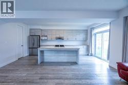 Contemporary kitchen featuring light wood-finish cabinetry, stainless steel appliances, a center island with a sink, and granite countertops - 
