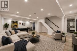 Spacious open-concept recreation area featuring light wood-finish flooring, recessed lighting, and a white painted staircase with a dark wood handrail - 