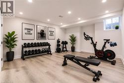 Dedicated fitness space featuring light wood-finish flooring, white walls, recessed ceiling lighting, and a window for natural illumination - 