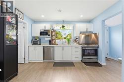 Bright kitchen featuring light wood-finish flooring, white cabinetry, a stainless steel range, and a stainless steel dishwasher - 
