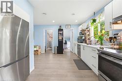 Kitchen featuring light wood-finish flooring, white cabinetry with silver hardware, a stainless steel refrigerator, a stainless steel range, and a window above the sink - 