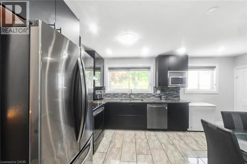 Kitchen featuring stainless steel appliances, dark cabinetry, light-toned tile flooring, dual windows, and a mosaic tile backsplash - 158 Plymouth Road, Kitchener, ON - Indoor Photo Showing Kitchen With Stainless Steel Kitchen With Upgraded Kitchen