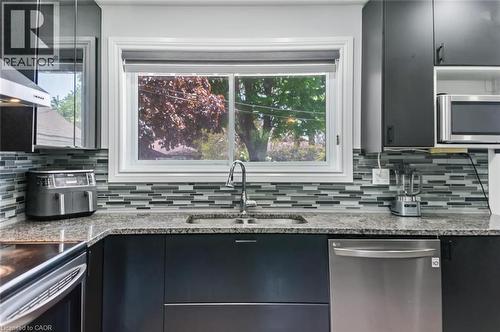 Contemporary kitchen featuring dark cabinetry, granite countertops, a stainless steel dishwasher, an undermount sink with a gooseneck faucet, and a multi-tone linear tile backsplash - 158 Plymouth Road, Kitchener, ON - Indoor Photo Showing Kitchen With Double Sink With Upgraded Kitchen