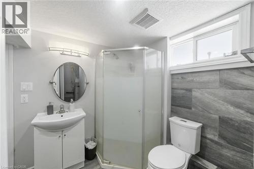 Bathroom featuring a corner shower with frosted glass enclosure, a white vanity with integrated sink, a round wall-mounted mirror, and a wall-mounted light fixture - 158 Plymouth Road, Kitchener, ON - Indoor Photo Showing Bathroom