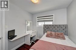 Bright room featuring a window with layered blinds, wood-finish flooring, a wall-mounted desk, and a built-in vanity with mirror - 