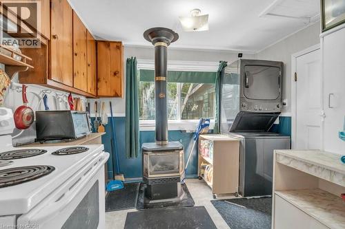 Functional kitchen space featuring a wood-burning stove, natural wood cabinetry, a white electric range, and a stacked washer and dryer unit - 1264 Parkinson Road, Woodstock, ON 