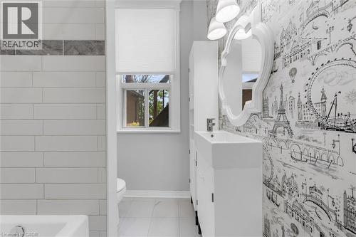 Bathroom featuring white subway tile, a decorative accent tile band, white vanity with integrated sink, contemporary wallpaper, and a wall-mounted mirror with overhead lighting - 205 Ferguson Avenue S, Hamilton, ON - Indoor Photo Showing Bathroom