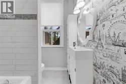 Bathroom featuring white subway tile, a decorative accent tile band, white vanity with integrated sink, contemporary wallpaper, and a wall-mounted mirror with overhead lighting - 