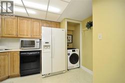 Functional utility area featuring wood-finish cabinetry, a built-in sink, a side-by-side refrigerator, and a dedicated laundry alcove with a washing machine - 