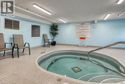 Indoor spa area featuring a tiled hot tub with a stainless steel handrail - 