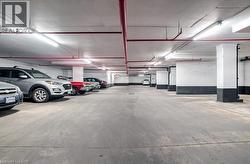 Spacious underground parking garage featuring concrete flooring, exposed red piping, and integrated fluorescent lighting - 