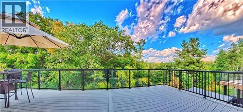 Spacious outdoor deck featuring composite decking, glass panel railing, and a lush tree canopy backdrop - 63 Ian Ormston Drive, Kitchener, ON - Outdoor With Deck Patio Veranda