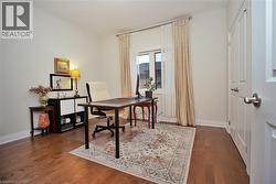 Bright interior room featuring wood-finish flooring, a white trim baseboard, and a window with light-colored drapery - 