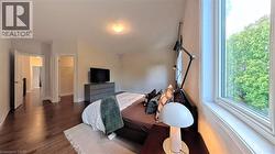 Spacious room featuring rich wood-finish flooring, a large window with white trim, and a built-in closet with shelving - 