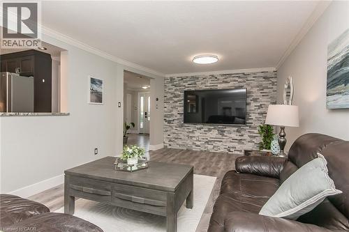 Living area with textured stone accent wall, recessed lighting, crown molding, wood-finish flooring, and a pass-through window to the kitchen - 529 Chesapeake Crescent, Waterloo, ON - Indoor Photo Showing Living Room