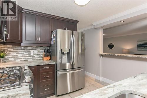 Stainless steel refrigerator and gas range, dark wood cabinetry, tile backsplash, and light-toned countertops - 529 Chesapeake Crescent, Waterloo, ON - Indoor Photo Showing Kitchen