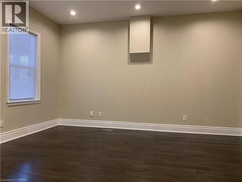 Spacious Unit 2 Living Room featuring wood-finish flooring, recessed ceiling lighting, a single window with blinds, and white trim baseboards - 405 Macnab Street N, Hamilton, ON 