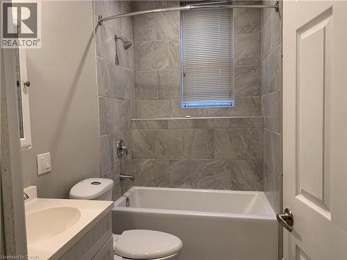 Unit 2 Bathroom featuring a white bathtub, light grey tiled shower surround with a built-in shelf, and a window with blinds - 405 Macnab Street N, Hamilton, ON 