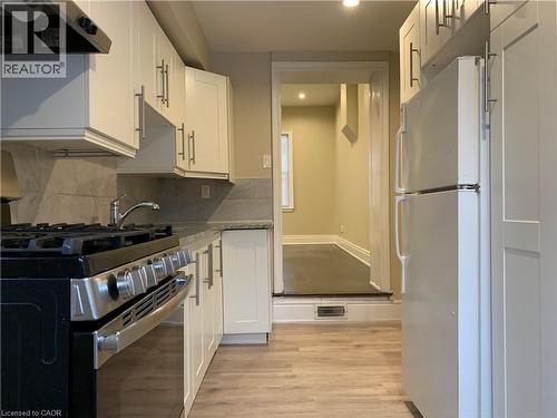 Unit 2 Kitchen featuring white shaker-style cabinetry, stainless steel gas range, coordinating stainless steel range hood, stone-finish countertops, and light wood-finish flooring - 405 Macnab Street N, Hamilton, ON 