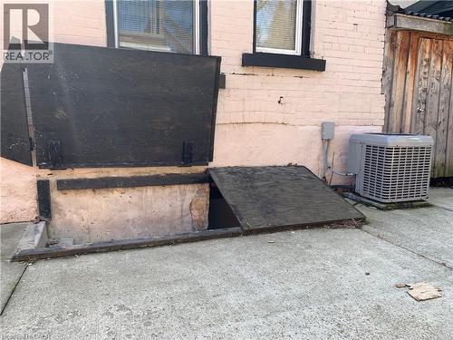 Concrete patio with a basement access hatch, painted brick exterior, and an exterior HVAC unit - 405 Macnab Street N, Hamilton, ON 