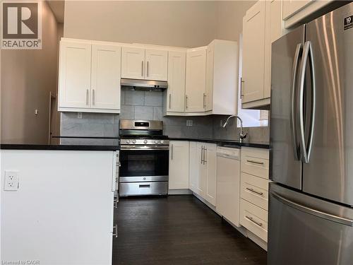 Unit 1 modern kitchen featuring white shaker cabinetry, stainless steel appliances, dark countertops, a grey tile backsplash, and dark wood-finish flooring - 405 Macnab Street N, Hamilton, ON 