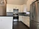Unit 1 modern kitchen featuring white shaker cabinetry, stainless steel appliances, dark countertops, a grey tile backsplash, and dark wood-finish flooring - 405 Macnab Street N, Hamilton, ON 