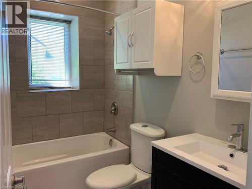 Unit 1 full bathroom featuring a white bathtub with a shower, complemented by beige tile surround - 405 Macnab Street N, Hamilton, ON 