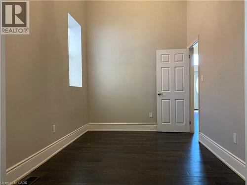 Unit 1 bedroom featuring wood-finish flooring, neutral wall paint, white trim, and a vertical window - 405 Macnab Street N, Hamilton, ON 