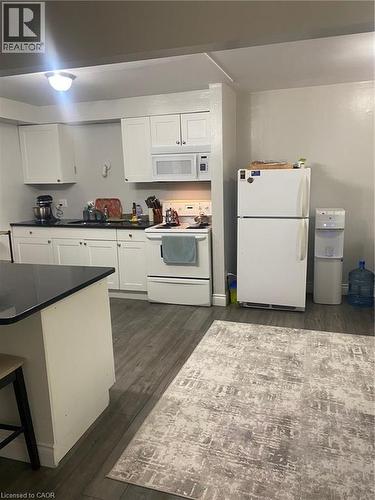 Kitchen with white range with electric cooktop, dark countertops, refrigerator, white cabinets, and dark wood-style flooring - 58 Hazelglen Drive, Kitchener, ON 