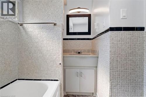 Bathroom featuring white square tile walls with black trim, a white vanity with integrated sink, a dark framed mirror, and an overhead vanity light - 14 Niagara Street, Hamilton, ON 